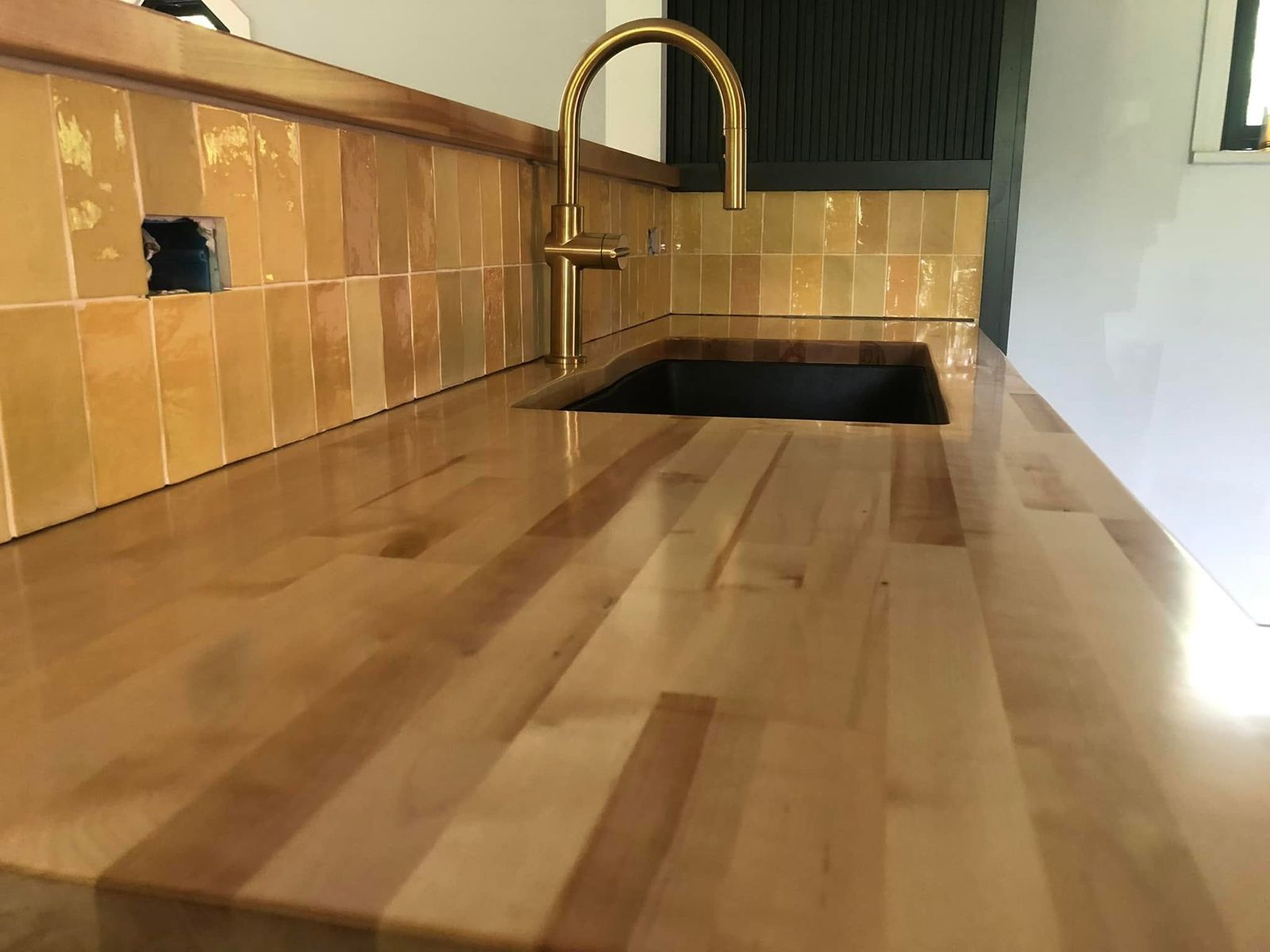 Maple butcher-block countertop with undermount black sink, brass faucet and glazed tile backsplash