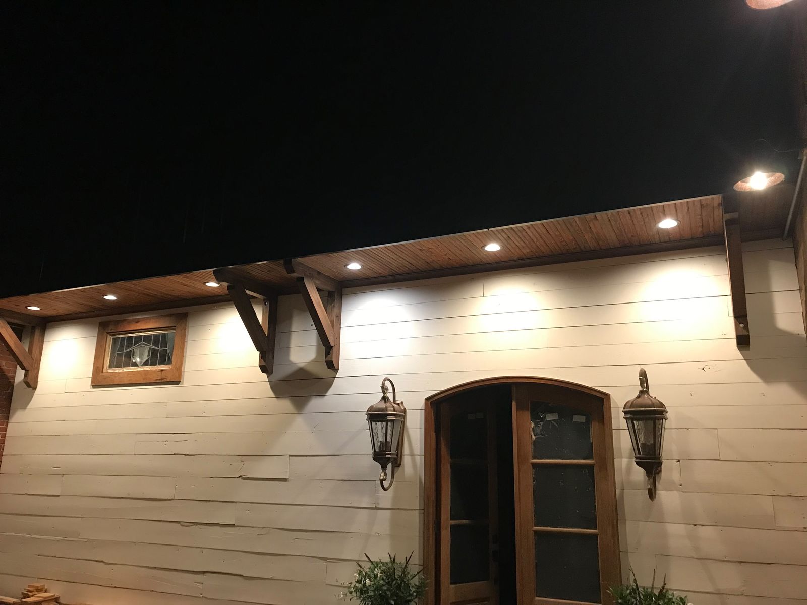 Arched entry with lantern sconces and wood soffit at night